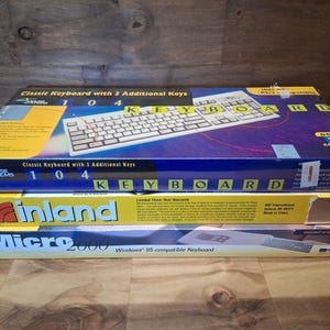 May include: Three stacked rectangular cardboard boxes containing computer keyboards. The top box is blue and yellow with the text Mouse Systems Classic Keyboard with 3 Additional Keys. The middle box is yellow with the Inland logo. The bottom box is white and blue with Micro 2000 Windows 95 compatible Keyboard text.