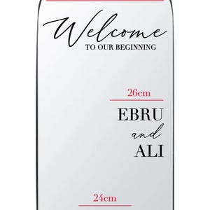 Peut inclure: Panneau blanc en forme d'arche avec texte noir. Il affiche "Welcome to our beginning", mesurant 45cm de large. En dessous, "Ebru and Ali" et "EA 29.06.2025". Le panneau mesure 26cm et 24cm de hauteur, respectivement.