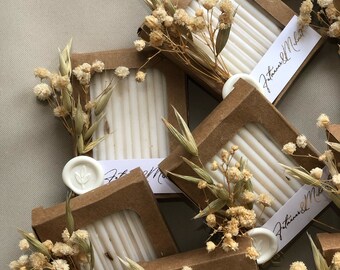May include: Small, brown boxes containing white soap bars. Each box features a white wax seal and dried flowers on top. The boxes are labelled with "J.Thomas & M.