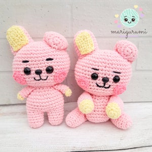 Puede incluir: Dos animales de peluche de crochet rosa con orejas amarillas y ojos negros. Los animales tienen una expresión sonriente con mejillas rosadas. Los animales están sentados sobre una superficie blanca. El texto "marigurummi" está en la esquina superior derecha de la imagen.