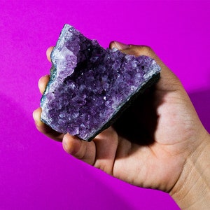 May include: A large amethyst crystal cluster with a deep purple colour. The crystal is in the shape of a cluster with many points.