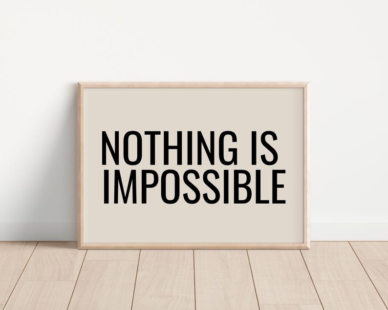 May include: A framed print with the words "NOTHING IS IMPOSSIBLE" in bold black letters. The background is a light beige color, and the frame is a light wood color. The print is displayed on a wooden floor.