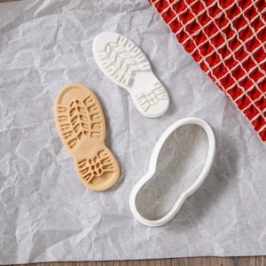 May include: Three cookie cutters in the shape of a footprint. Two are white and one is brown.