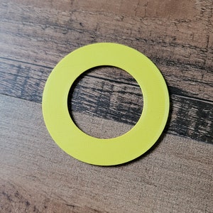 May include: A bright yellow, circular object with a hole in the center. The object has a textured surface and is set against a wooden background. The shape is a ring.