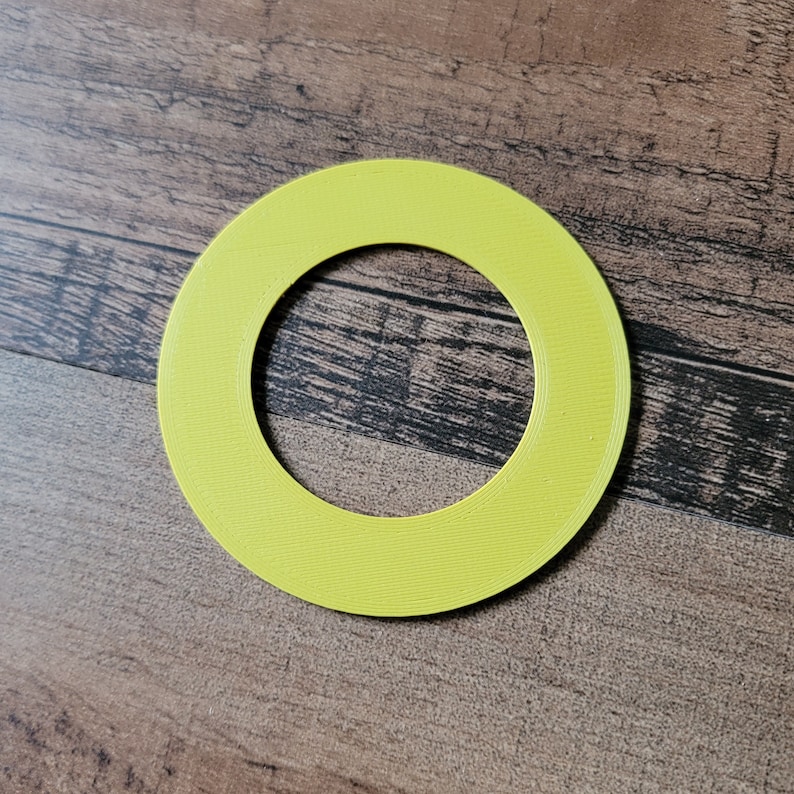 May include: A bright yellow, circular object with a hole in the center. The object has a textured surface and is set against a wooden background. The shape is a ring.