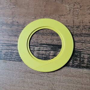 May include: A bright yellow, circular object with a hollow center. The object has a layered design and a textured surface. The item is set against a wooden background.