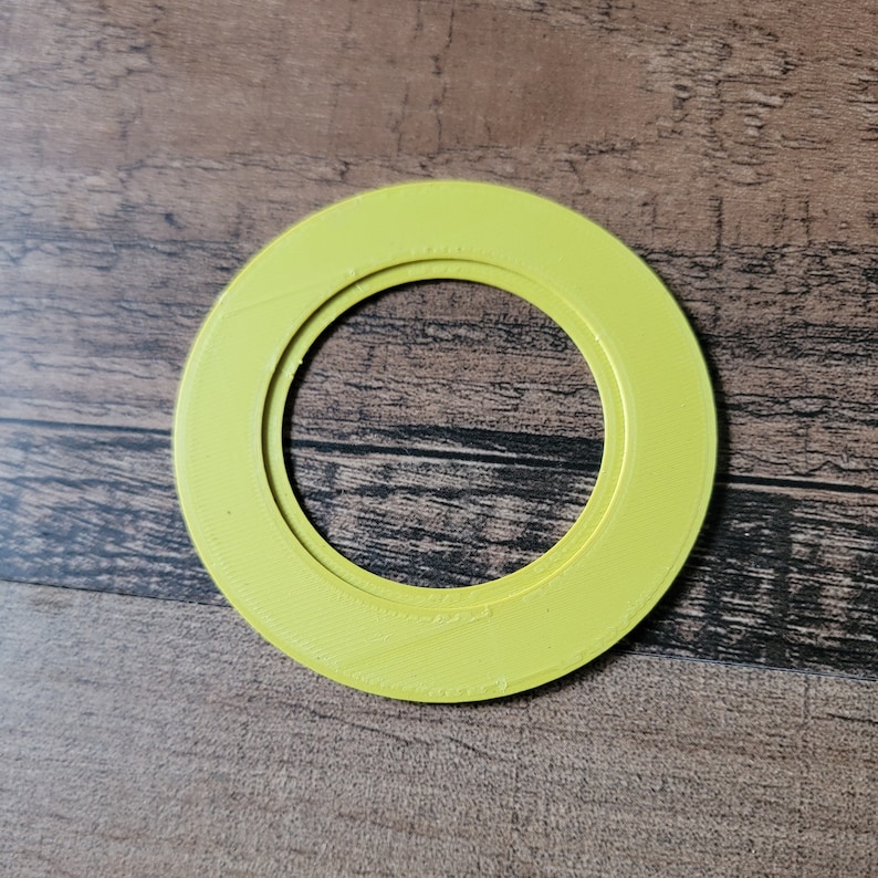 May include: A bright yellow, circular object with a hollow center. The object has a layered design and a textured surface. The item is set against a wooden background.