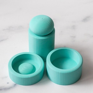 May include: Three turquoise blue 3D printed molds for resin casting. The molds are cylindrical with a rounded top and a flat bottom. The molds are designed to create a dome, a cylinder, and a smaller cylinder.
