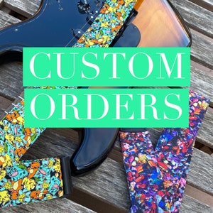 May include: Two guitar straps with colorful patterns. One strap features a blue, yellow, and green pattern with cartoon characters. The other strap features a multi-colored pattern with a variety of characters. The text "CUSTOM ORDERS" is superimposed on the image.