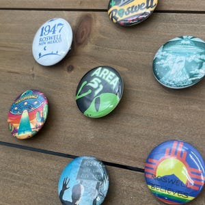 Peut inclure: Une collection de dix badges bouton de 2,5 cm de diam&egrave;tre avec diff&eacute;rents motifs li&eacute;s &agrave; Roswell, au Nouveau-Mexique et aux OVNIS. Les badges pr&eacute;sentent des images de soucoupes volantes, d'extraterrestres et du texte qui dit "1947 Roswell Nouveau-Mexique", "Roswell", "Zone 51", "Limite de la ville de Roswell Elev 3570", et "Roswell croit".