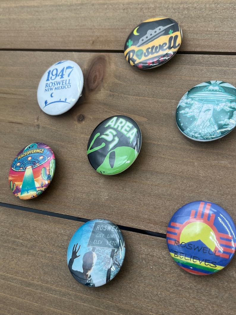 Peut inclure: Une collection de dix badges bouton de 2,5 cm de diam&egrave;tre avec diff&eacute;rents motifs li&eacute;s &agrave; Roswell, au Nouveau-Mexique et aux OVNIS. Les badges pr&eacute;sentent des images de soucoupes volantes, d'extraterrestres et du texte qui dit "1947 Roswell Nouveau-Mexique", "Roswell", "Zone 51", "Limite de la ville de Roswell Elev 3570", et "Roswell croit".