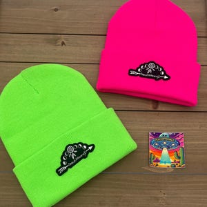 May include: Two neon green and pink knitted beanies with a black and white patch that says "Peace Offeringz" and a dreamcatcher design. A sticker with a UFO and the text "Peace Offeringz" is also shown.