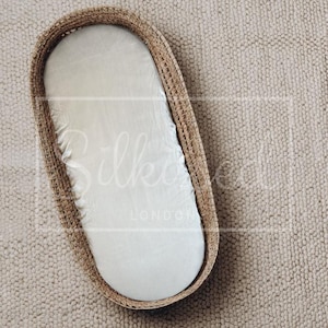 Pode incluir: Uma cesta oval tecida com interior branco e lençol branco com elástico. A cesta é feita de material tecido de cor natural. O produto é projetado para bebês.