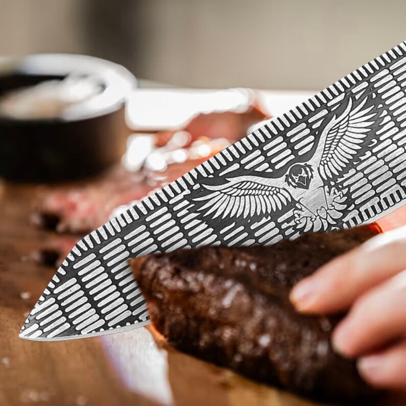 K&ouml;nnte beinhalten: Nahaufnahme eines silbernen Messers mit einem Muster eines Vogels mit ausgebreiteten Fl&uuml;geln. Das Messer schneidet in ein St&uuml;ck gekochtes Fleisch.