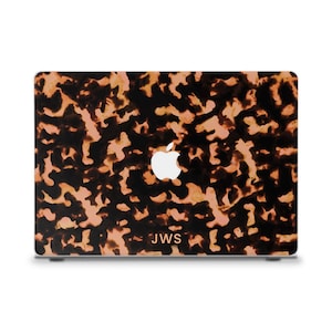 May include: A laptop computer with a tortoiseshell pattern case. The case has a mottled design in shades of brown and tan. The Apple logo is visible, and the initials "JWS" are printed below it.