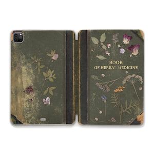 May include: A green book with a worn leather cover and dried flowers pressed into the pages. The title on the cover reads "Book of Herbal Medicine".