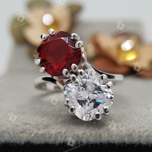 Peut inclure: Une bague en argent ornée de deux pierres précieuses. L'une est une grosse pierre rouge foncé de forme ronde, l'autre est une pierre transparente en forme de cœur. La bague a un design unique.