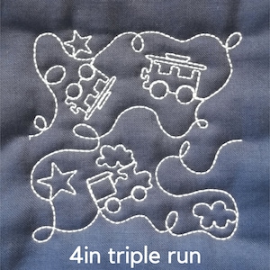 May include: A white stitched design on a dark blue fabric background. The design features a train, stars, and swirls. The text "4 in triple run" is at the bottom of the image.