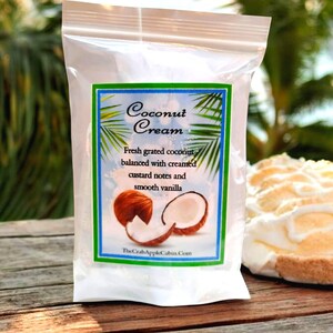 May include: A white resealable bag with a label that reads "Coconut Cream" and features a description of the product: "Fresh grated coconut balanced with creamed custard notes and smooth vanilla". The label also includes a picture of a coconut cut in half and a piece of coconut.