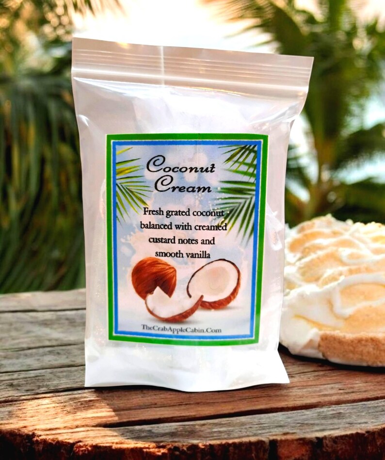 May include: A white resealable bag with a label that reads "Coconut Cream" and features a description of the product: "Fresh grated coconut balanced with creamed custard notes and smooth vanilla". The label also includes a picture of a coconut cut in half and a piece of coconut.