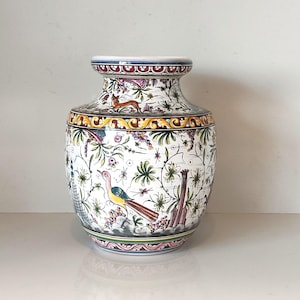 May include: A decorative ceramic vase with a white base and colorful floral and bird designs. The vase features a wide body, a narrow neck, and a flared rim. The design includes a variety of colors, including blue, yellow, green, and pink.