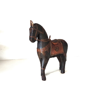Pode incluir: Estatueta de cavalo de madeira castanha escura com sela e freio. A sela é castanha clara com detalhes decorativos. O cavalo tem um design detalhado e está em quatro patas. A estatueta é um item decorativo.
