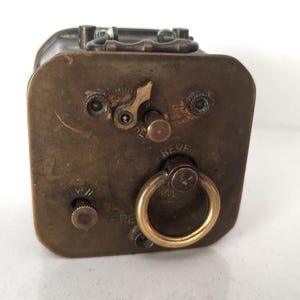 K&ouml;nnte beinhalten: Antike Metallbox in Messingfarbe mit rechteckiger Form. Die Box hat einen Klappdeckel, einen kreisf&ouml;rmigen Griff und verschiedene Zifferbl&auml;tter und Hebel. Das Wort "REVE" ist auf einem Zifferblatt zu sehen. Die Box hat ein Vintage-Aussehen.