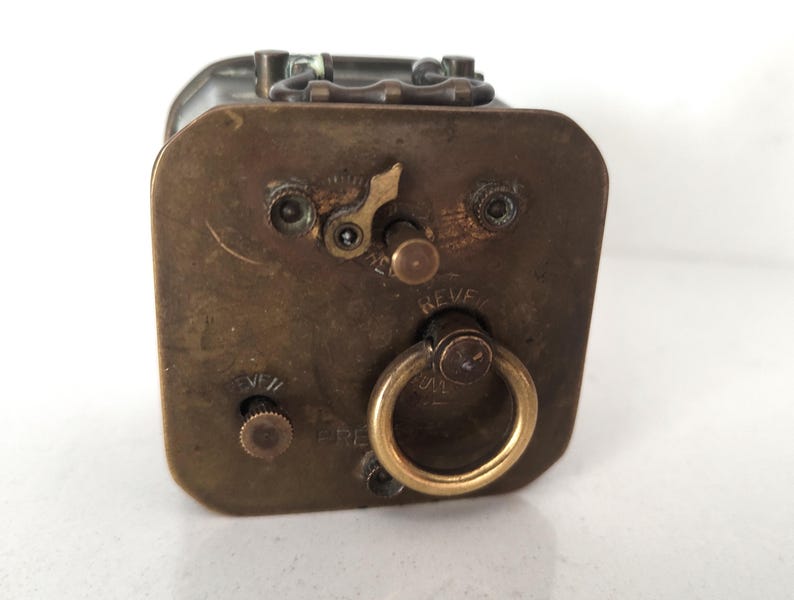 K&ouml;nnte beinhalten: Antike Metallbox in Messingfarbe mit rechteckiger Form. Die Box hat einen Klappdeckel, einen kreisf&ouml;rmigen Griff und verschiedene Zifferbl&auml;tter und Hebel. Das Wort "REVE" ist auf einem Zifferblatt zu sehen. Die Box hat ein Vintage-Aussehen.