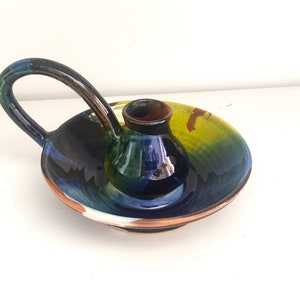 May include: A ceramic candle holder with a blue, green and yellow glaze. The holder has a handle and a small, round base.