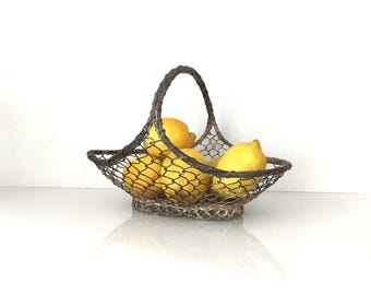 Puede incluir: Una cesta de alambre con asa, llena de limones amarillos brillantes. La cesta tiene un aspecto oscuro y envejecido. Los limones están maduros y frescos, creando un contraste vibrante. La cesta está sobre una superficie blanca.