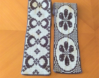 May include: Two rectangular, decorative textile pieces with a repeating pattern. The design features alternating shapes of circles and floral motifs in a dark purple color against a light beige background. The textiles are likely handmade and suitable for home decor.