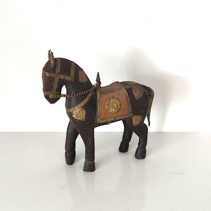 Könnte beinhalten: Eine Holzpferdefigur mit brauner und schwarzer Bemalung. Das Pferd ist mit goldenen und messingfarbenen Akzenten verziert, darunter ein Sattel und ein Zaumzeug.