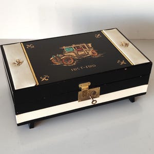May include: Black rectangular box with a hinged lid, featuring a vintage car illustration and the text "1915 T-FORD." The box has gold accents, a lock, and a key. The sides are black and white.
