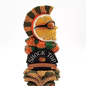 May include: A Shock Top Pumpkin Wheat beer tap handle featuring a cartoon orange with sunglasses and a mohawk, surrounded by pumpkins and wheat stalks.