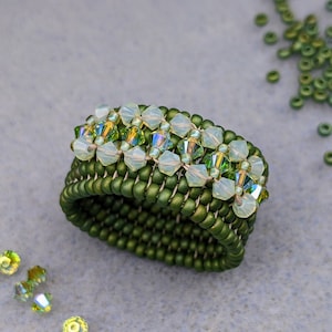 Könnte beinhalten: Ein grüner Perlenring mit einer Reihe von schillernden grünen und weißen Perlen.