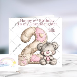May include: A square greeting card featuring the text Happy 2nd Birthday To my Granddaughter Hattie. The design includes a large number two with a stitched fabric pattern in beige and pink, a small gift box, and a fluffy gray teddy bear holding a pink heart.