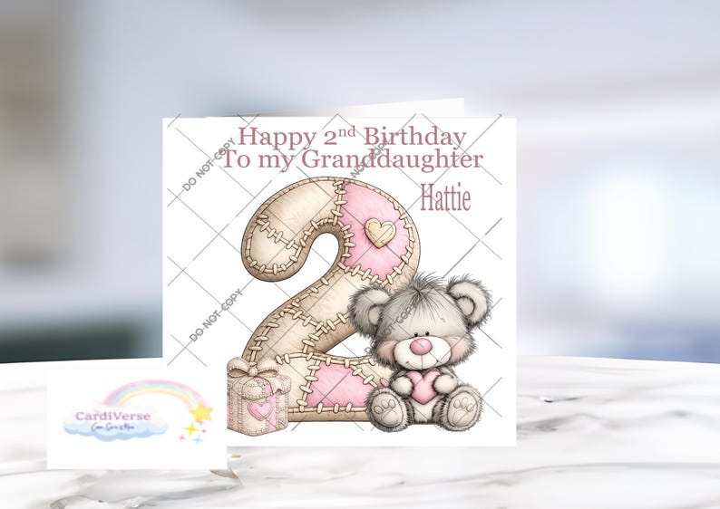 Może przedstawiać: Kwadratowa kartka okolicznościowa z napisem Happy 2nd Birthday To my Granddaughter Hattie. Projekt zawiera dużą cyfrę dwa z wzorem szytej tkaniny w kolorze beżowym i r&oacute;żowym, małe pudełko prezentowe oraz puszystego szarego misia z r&oacute;żowym sercem.