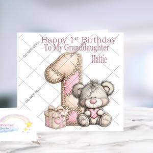 May include: A square greeting card featuring the text Happy 1st Birthday To My Granddaughter Hattie. The design includes a large beige and pink number one with stitched details, a small gift box, and a fluffy gray teddy bear holding a pink heart.