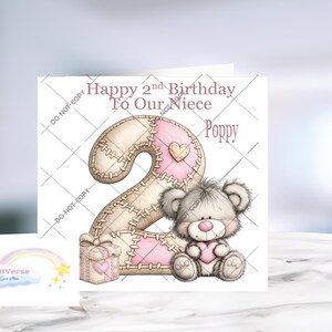 Może przedstawiać: Kwadratowa kartka okolicznościowa z napisem Happy 2nd Birthday To Our Niece Poppy. Projekt zawiera dużą cyfrę dwa z przeszywanym wzorem patchworkowym w kolorze beżowym i r&oacute;żowym, małe pudełko prezentowe oraz puszystego szarego misia z r&oacute;żowym sercem.