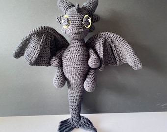May include: A black crocheted dragon with yellow eyes. The dragon has wings and a long tail.