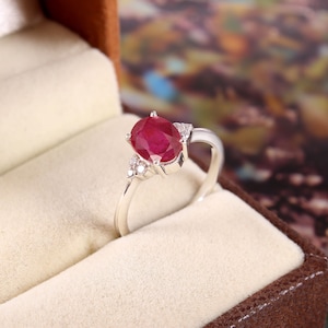 May include: A silver ring featuring a large oval ruby gemstone with smaller diamond accents.
