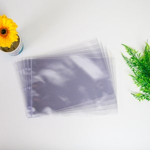 May include: A stack of clear plastic sheet protectors with holes punched along the left side. The sheet protectors are stacked on a white surface.