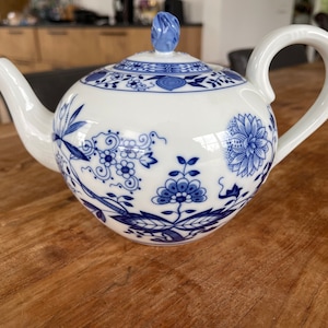 Puede incluir: Tetera de porcelana blanca con diseños florales azules. La tetera tiene un pico curvo, un cuerpo redondeado y un asa en forma de lazo. La tapa está rematada con un pomo azul. Incluye motivos florales y de hojas azules detallados.