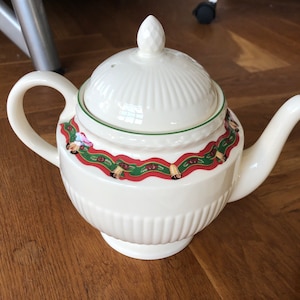 Pode incluir: Bule de chá de cerâmica branca com um design de Natal verde e vermelho. A chaleira tem uma tampa com uma pega no topo.