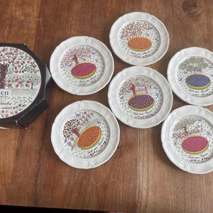 Könnte beinhalten: Ein Set aus sechs weißen Keramik-Cocktailtellern von Gien France, die jeweils mit einer Obsttorten-Illustration und einem Baummotiv verziert sind. Die Teller befinden sich in einer schwarzen achteckigen Schachtel mit der Aufschrift Gien France Les Tartes.