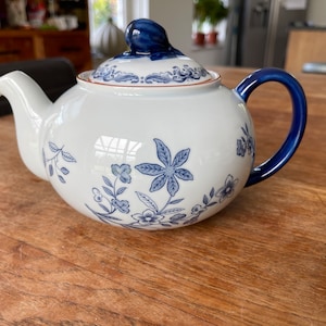 May include: A white teapot with a blue and white floral design. The teapot has a blue lid and a blue handle.