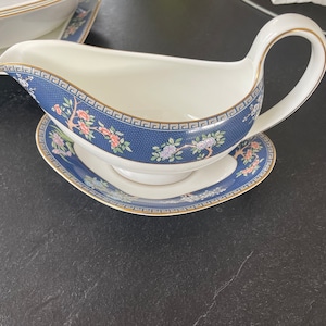 May include: White porcelain gravy boat with a matching saucer. The boat and saucer feature a navy blue border with a floral and geometric design, accented with gold trim. A classic addition to any dining set.
