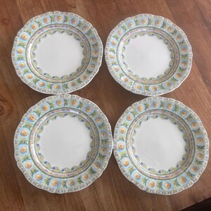 May include: Set of four white ceramic plates with a blue, green, and yellow floral design. The plates have a scalloped edge.