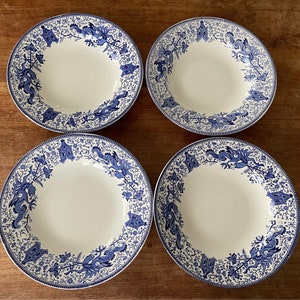 May include: Four white soup bowls with blue and white floral and dragon designs. The bowls are arranged in a square pattern on a wooden surface.