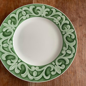 May include: A white ceramic dinner plate with a green floral design around the rim.